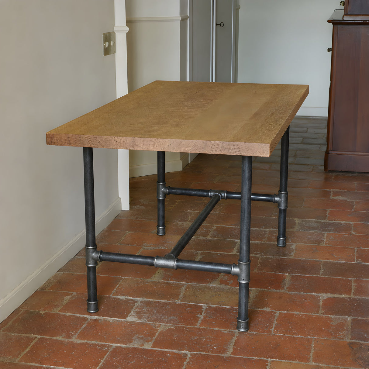 H-frame dining table base, cast iron and varnished steel Ø 34 mm, shown in a room under a raw sawn oak tabletop