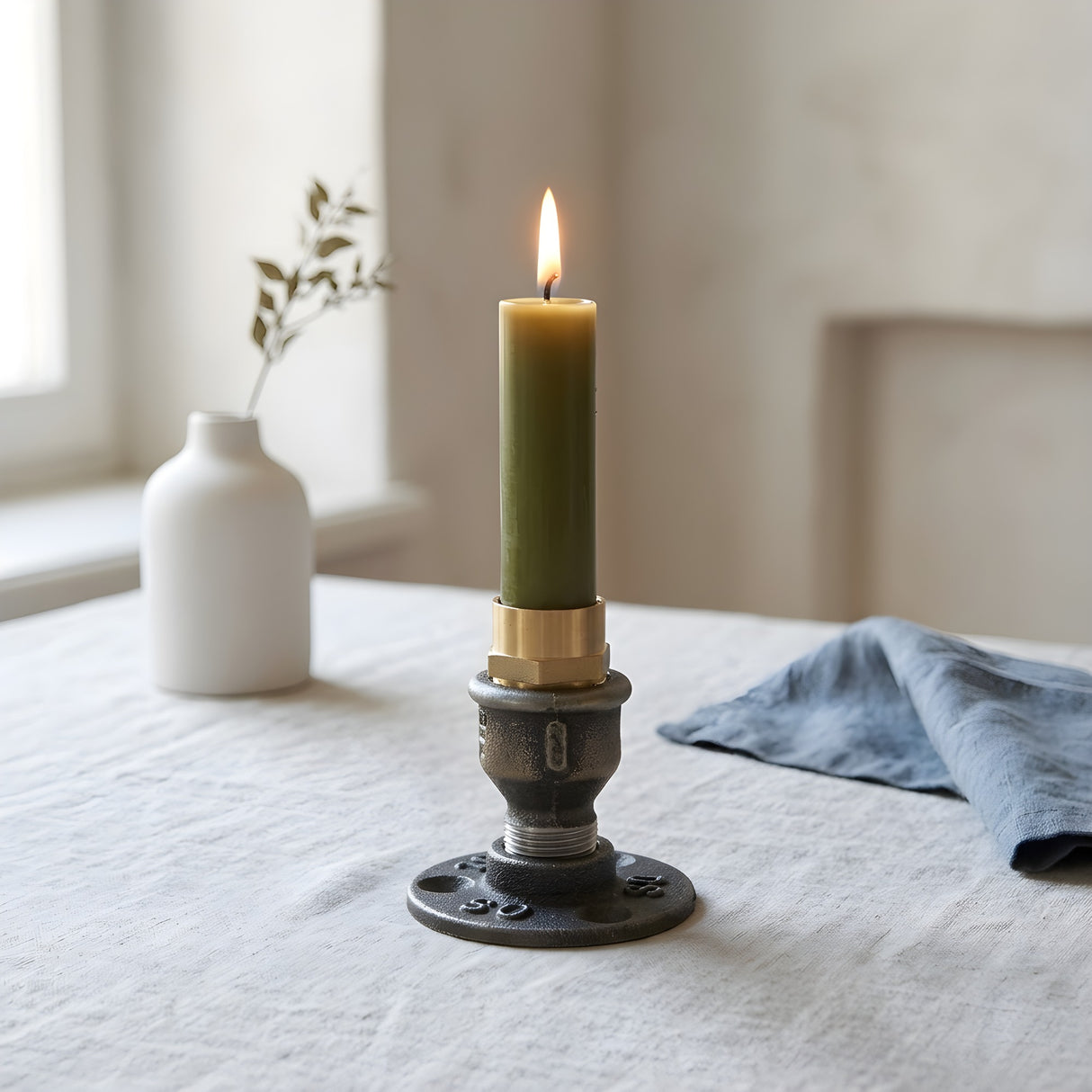 Petit bougeoir industriel en fonte et laiton avec bougie allumée sur une table