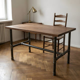 H-frame dining table base, cast iron and varnished steel Ø 34 mm, shown in a room under a solid walnut tabletop