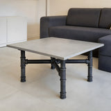 Cross-leg coffee table base, cast iron and varnished steel Ø 42 mm, shown in a room under a pale polished concrete tabletop