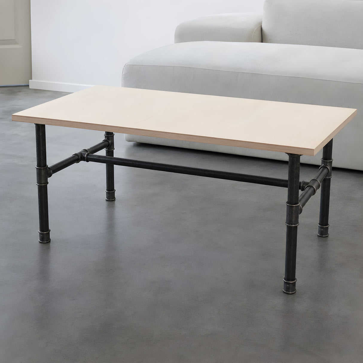 H-frame coffee table base, cast iron and varnished steel Ø 27 mm, shown in a room under a birch plywood tabletop
