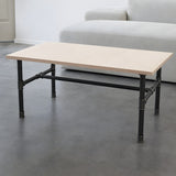 H-frame coffee table base, cast iron and varnished steel Ø 27 mm, shown in a room under a birch plywood tabletop