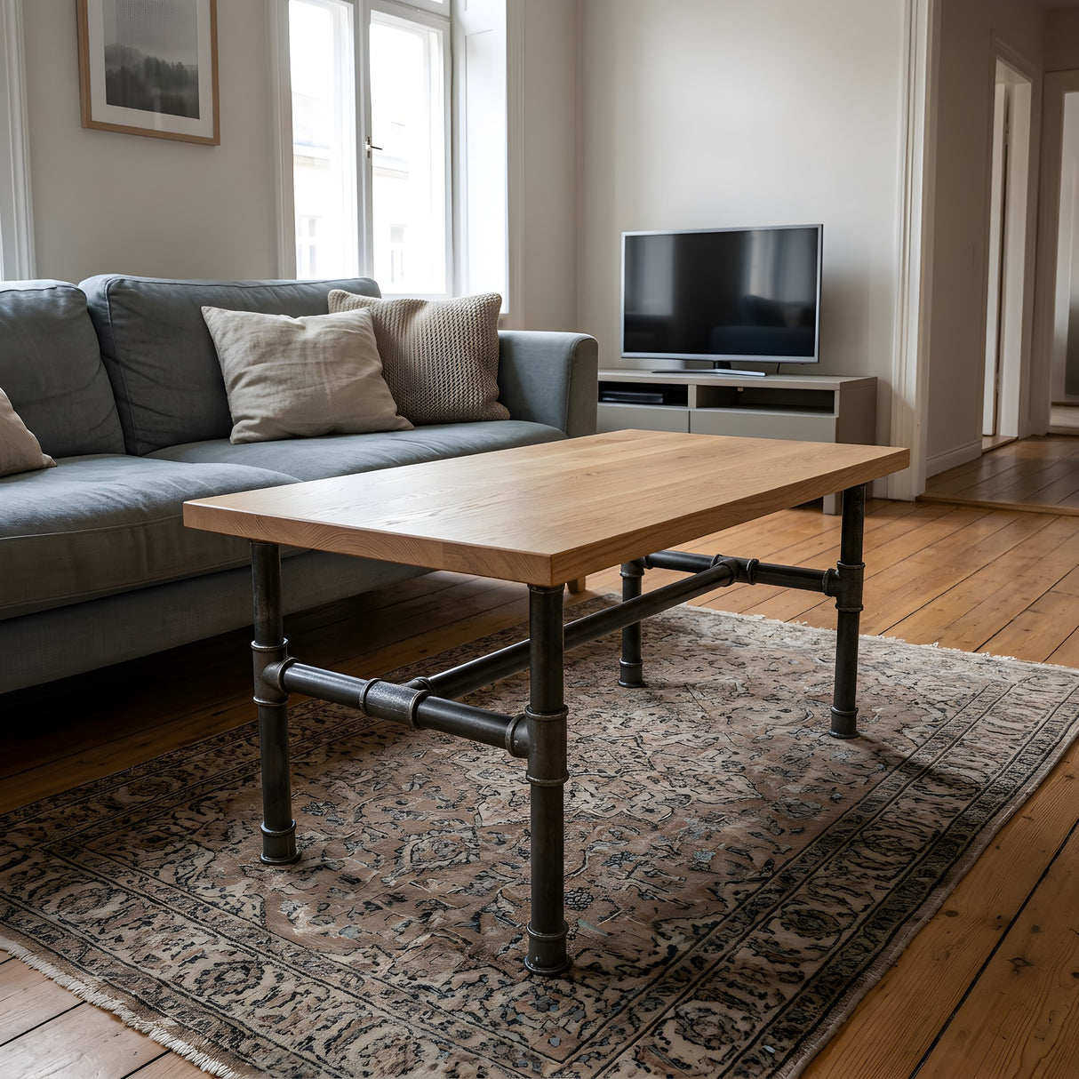 H-frame coffee table base, cast iron and varnished steel Ø 34 mm, shown in a room under a light solid oak tabletop