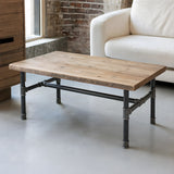 H-frame coffee table base, cast iron and varnished steel Ø 34 mm, shown in a room under a reclaimed pine tabletop