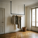 Ceiling-hung black pipe clothes rail in an entrance hall, a coat and a scarf hanging from it